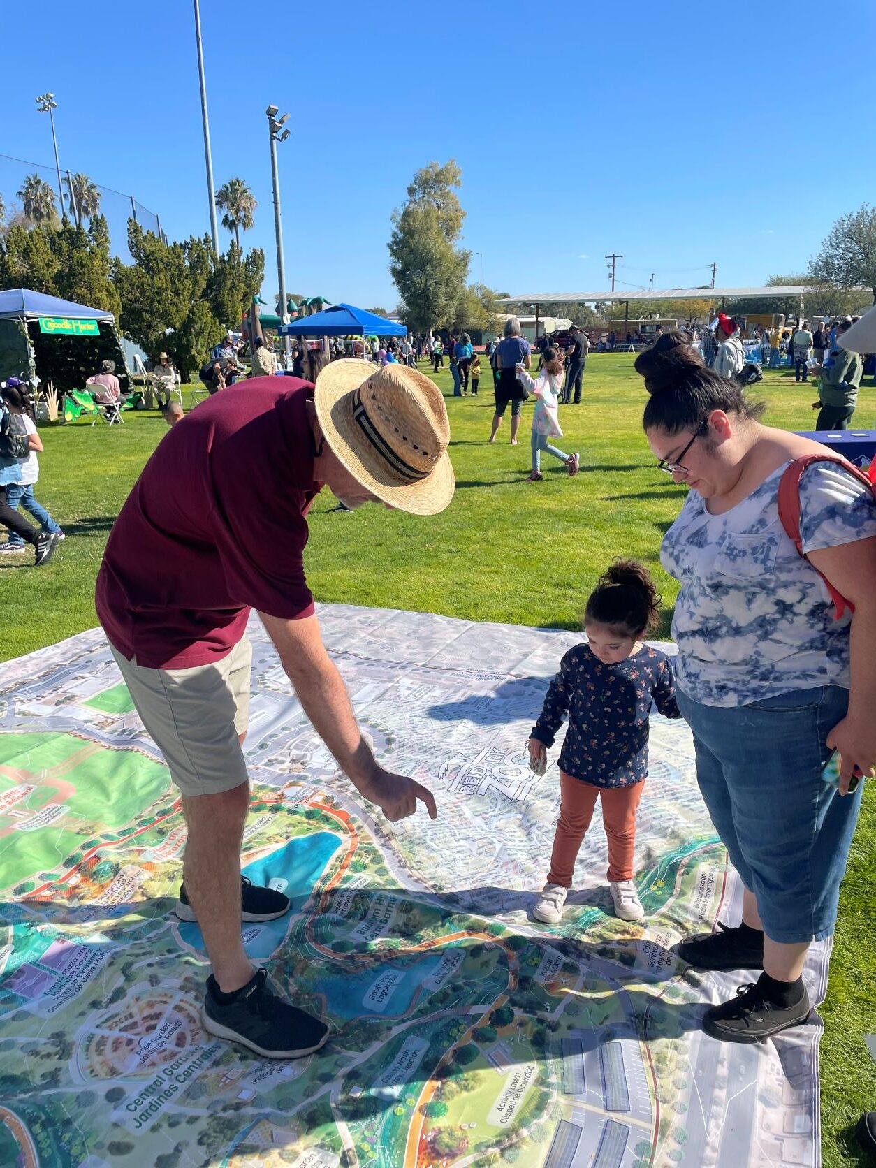 Family fest event with design team member standing on large site plan and pointing while explaining to a community member with her child