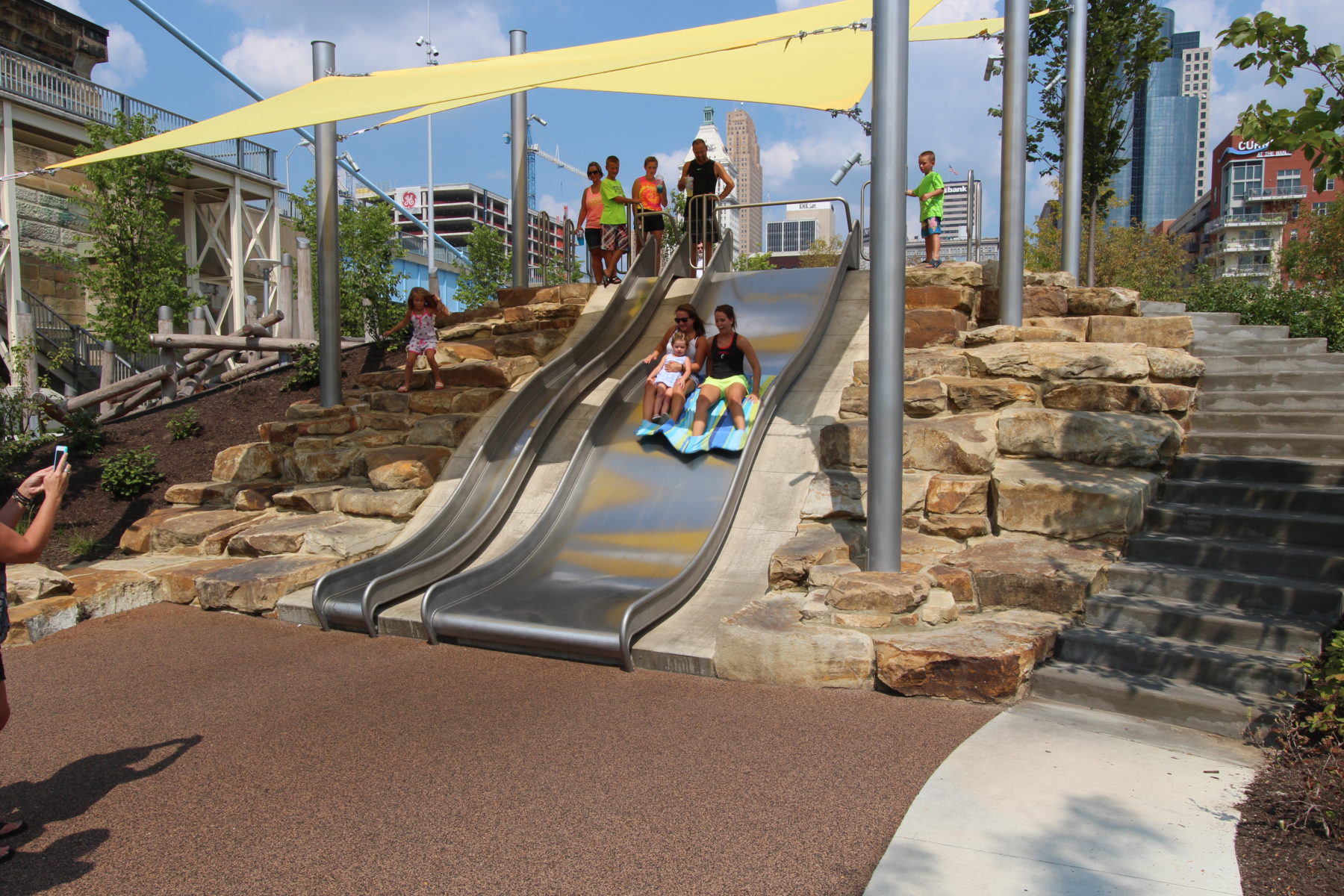 Two women going down large metal slide with a toddler