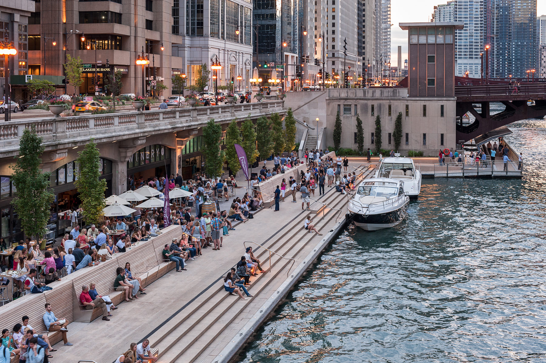 People sitting on stairs in front of Chicago Riverwalk, boats parked alongside them