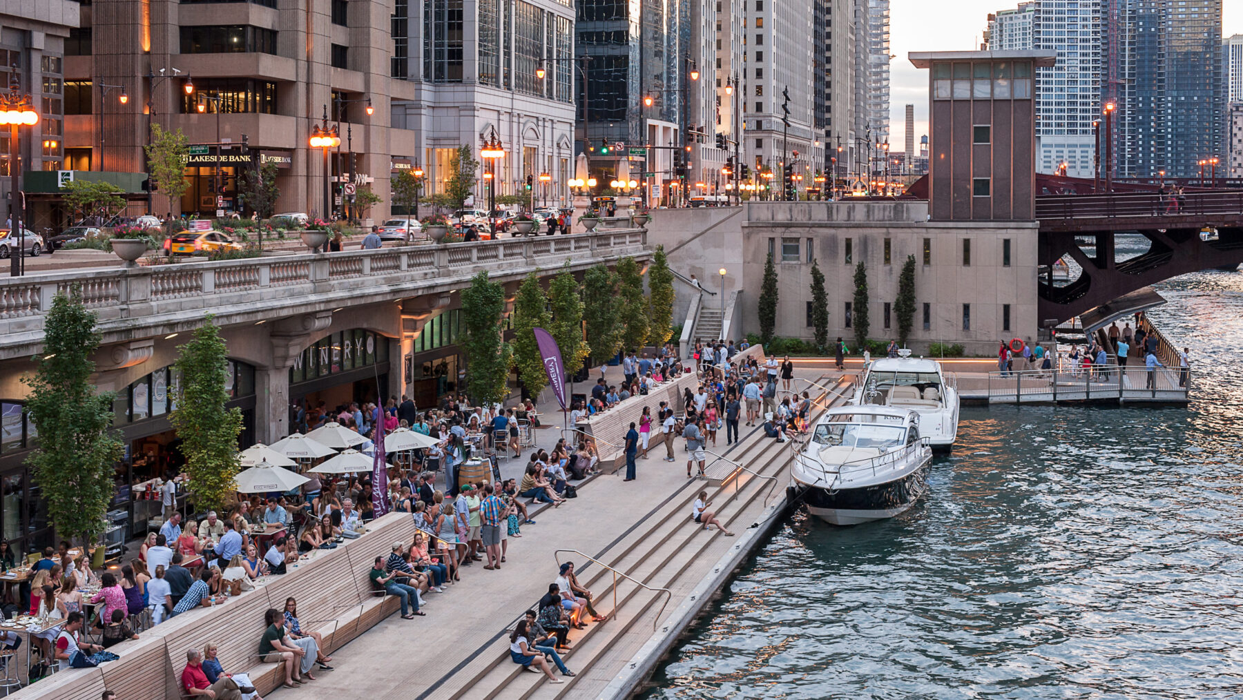People sitting on stairs in front of Chicago Riverwalk, boats parked alongside them