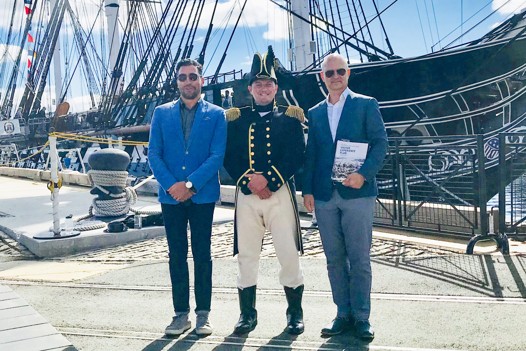 three men stand in front of a ship