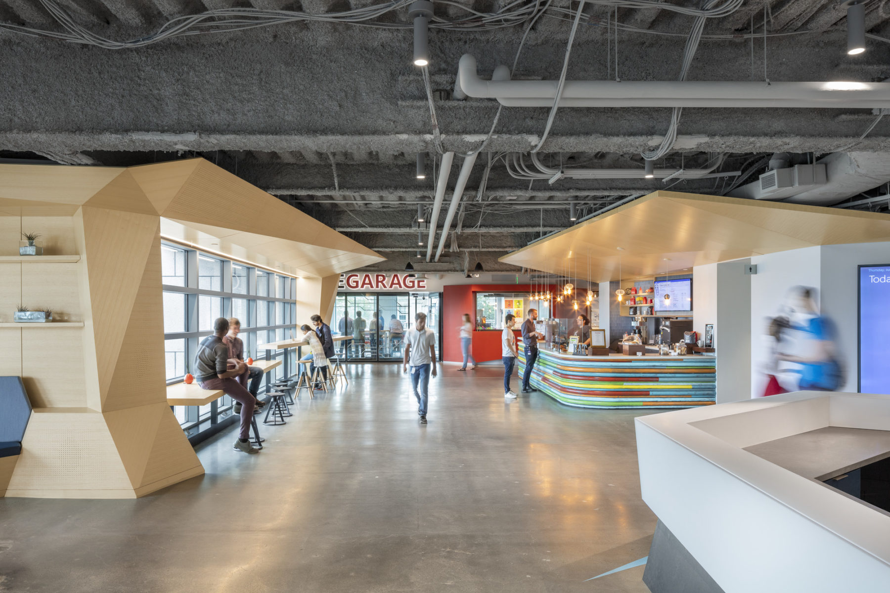 Person walks down open walkway of NERD center which has colorful, light-filled collaboration spaces on each side