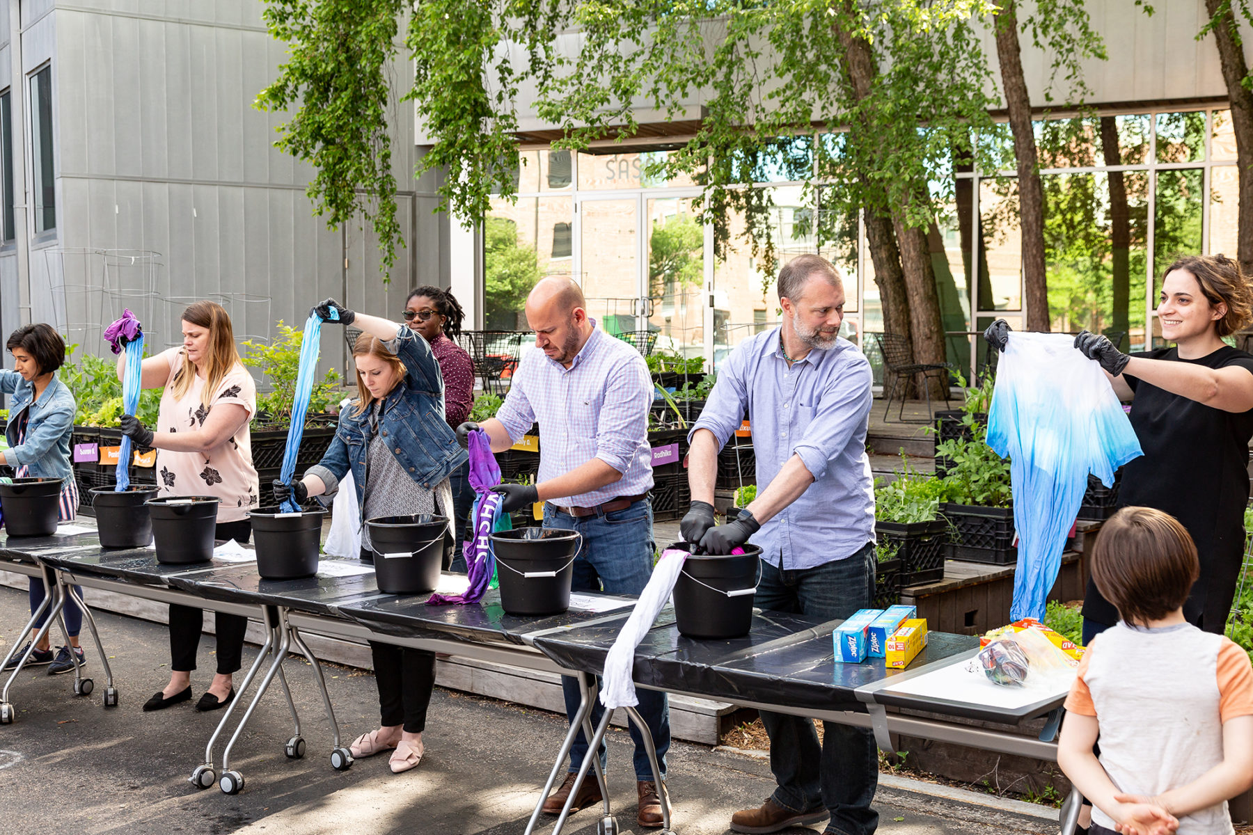 Photo of people lined up at tables with buckets tie-dying shirts