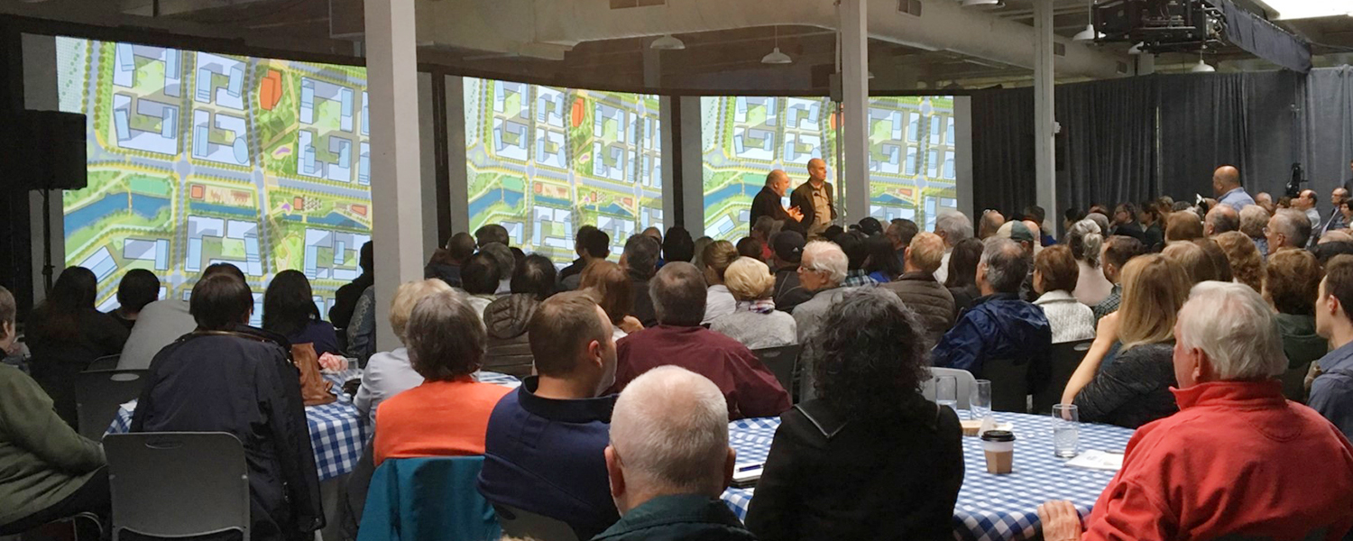 People sitting in an audience listening to two designers present at the front of the room