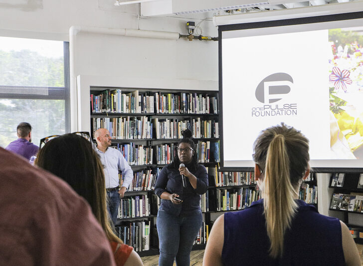 Speaker presenting to audience. The One Pulse Foundation logo is on screen