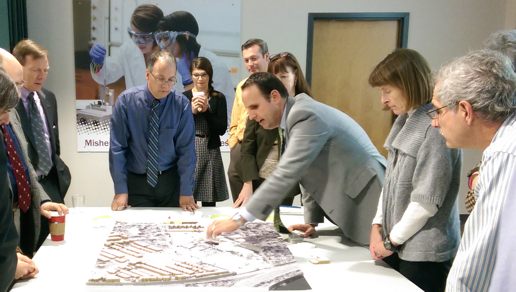 A planner points to a map model on the table while clients look on