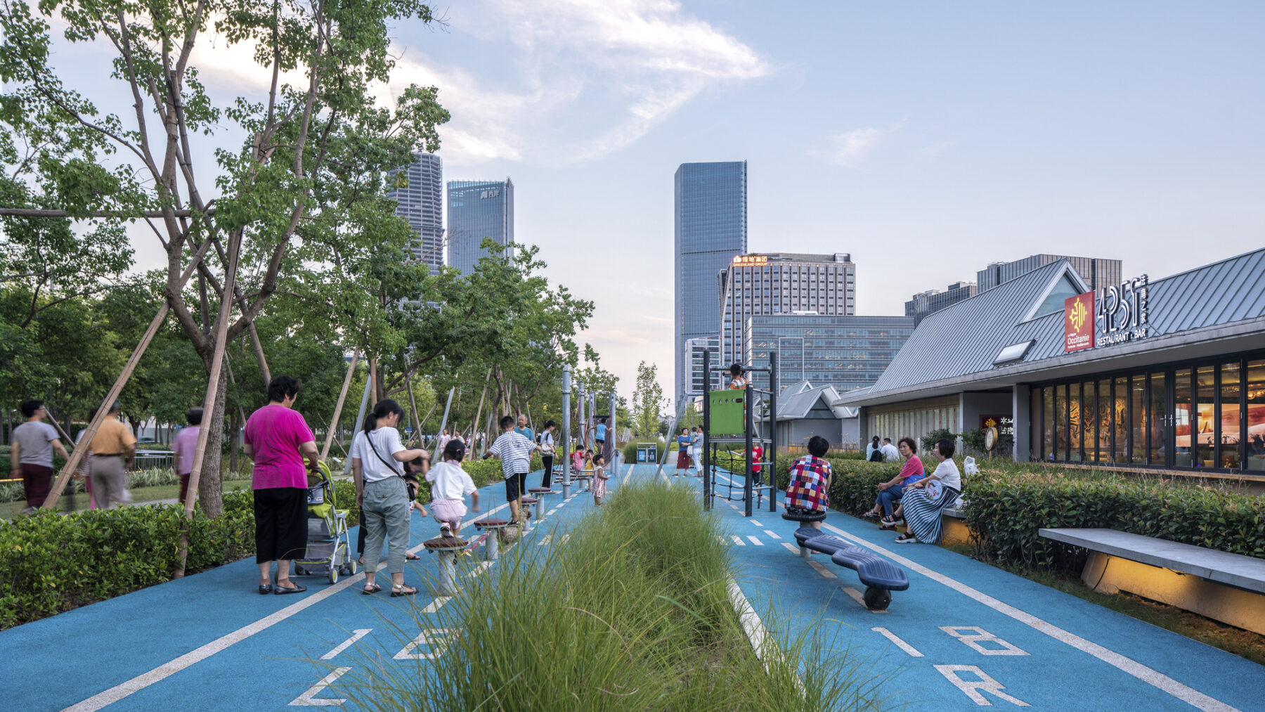 Walkway with playscape elements, children climbing, and pedestrians walking with the city high rise buildings in background