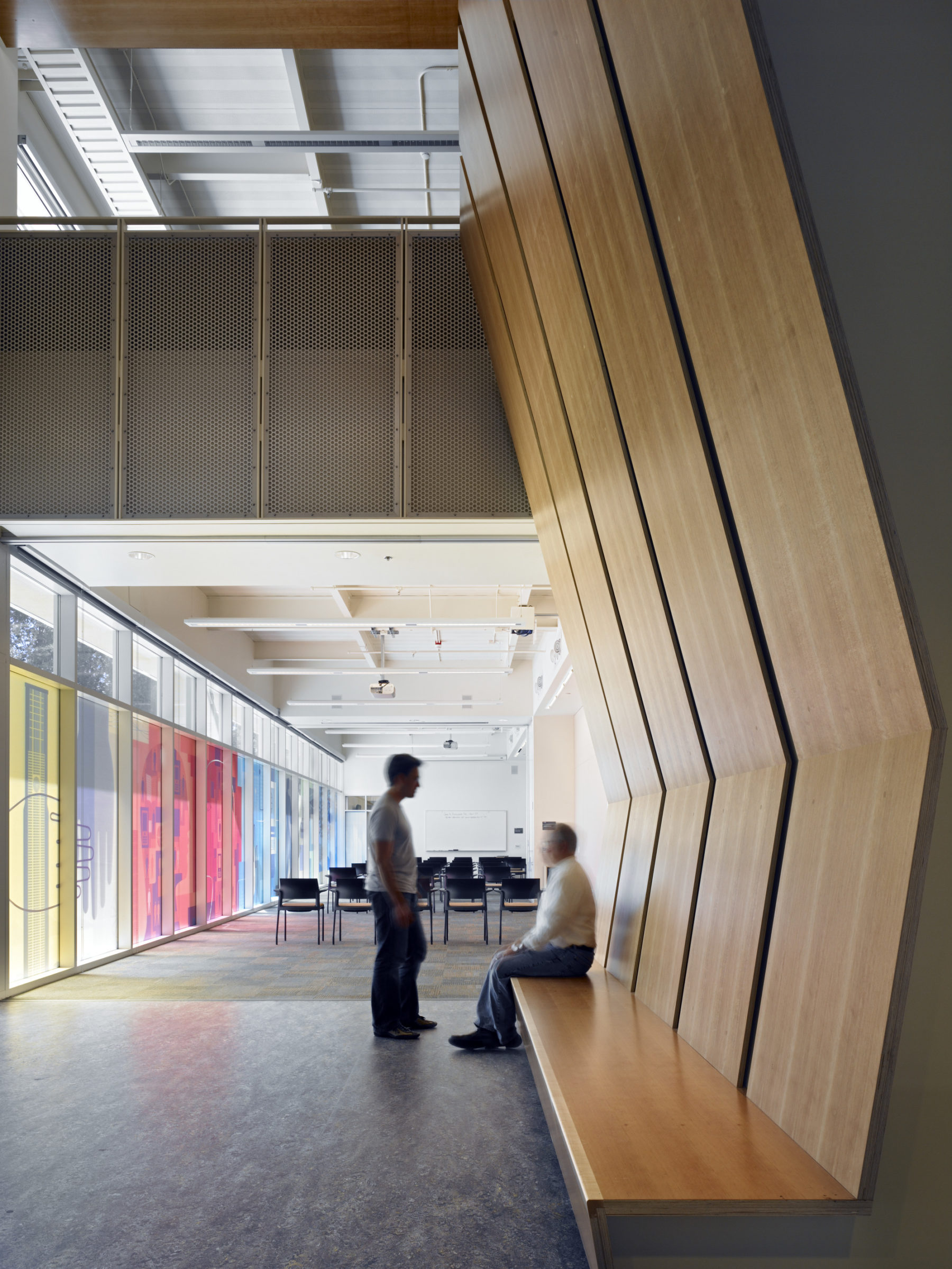 Interior photo of two men chatting. One is sitting on a built in bench