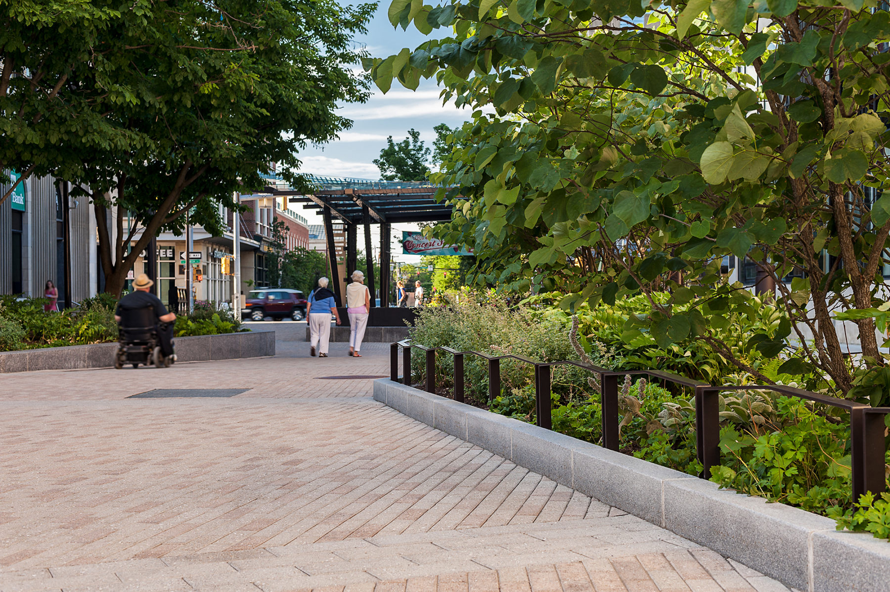 Pedestrians walking down a stone walkway lined with trees and greenery