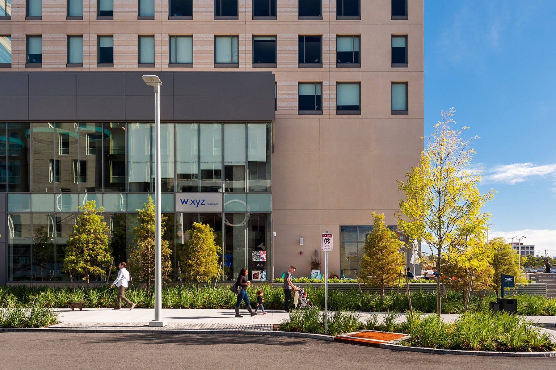 Elevational photo of the built hotel. People walk along the sidewalk in front of it.