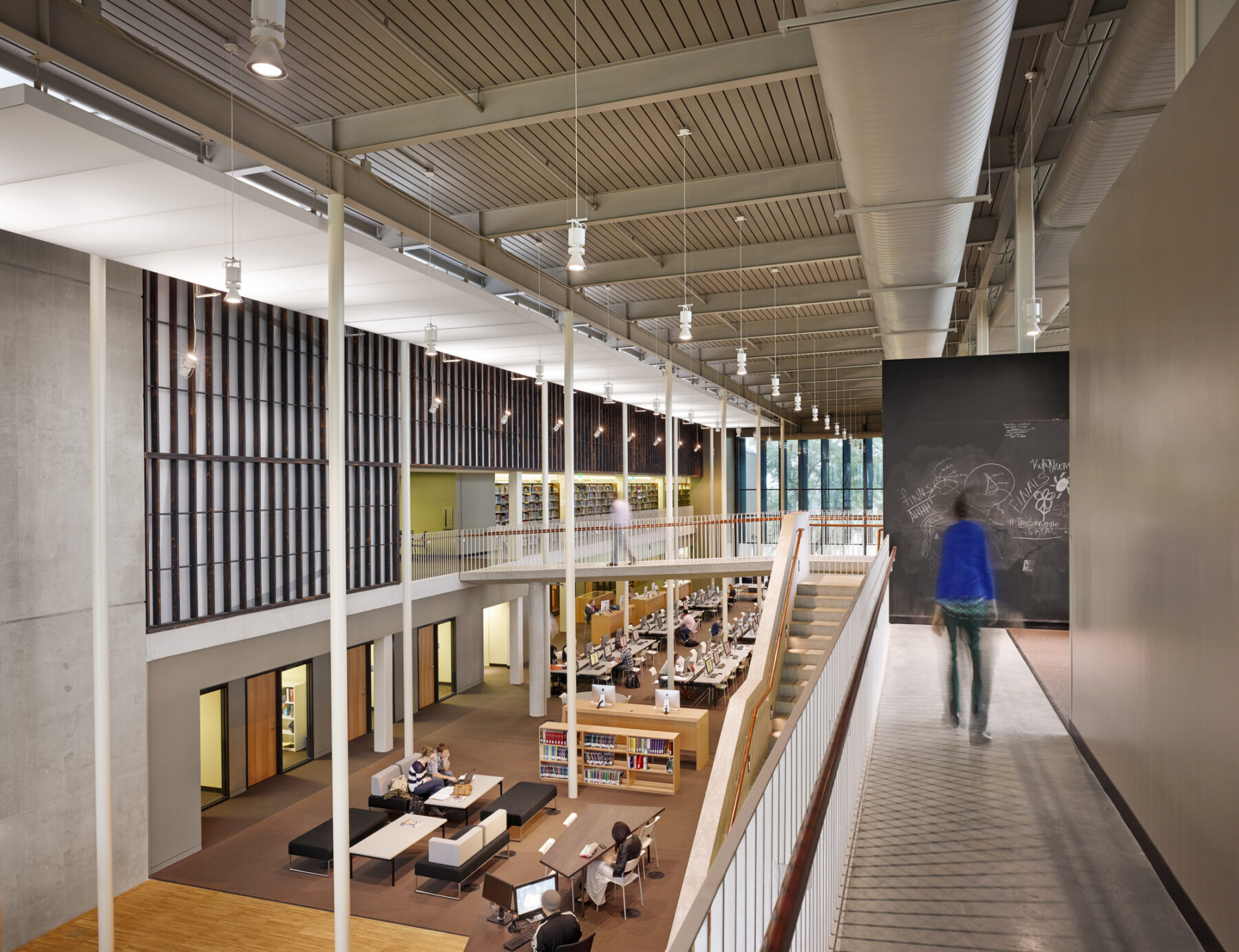 perspective photograph of student walking along second floor corridor overlooking library main room