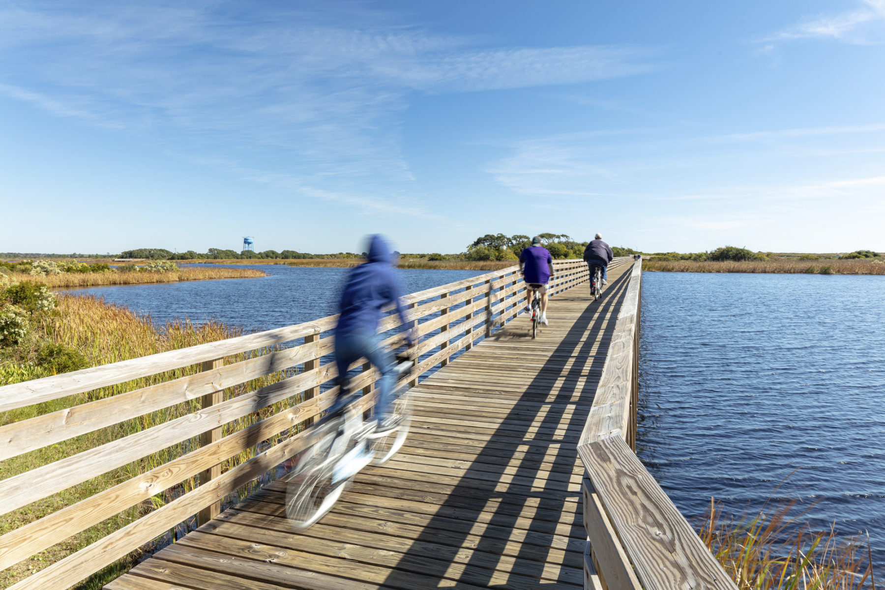 photo of people running and biking on a boardwalk across water