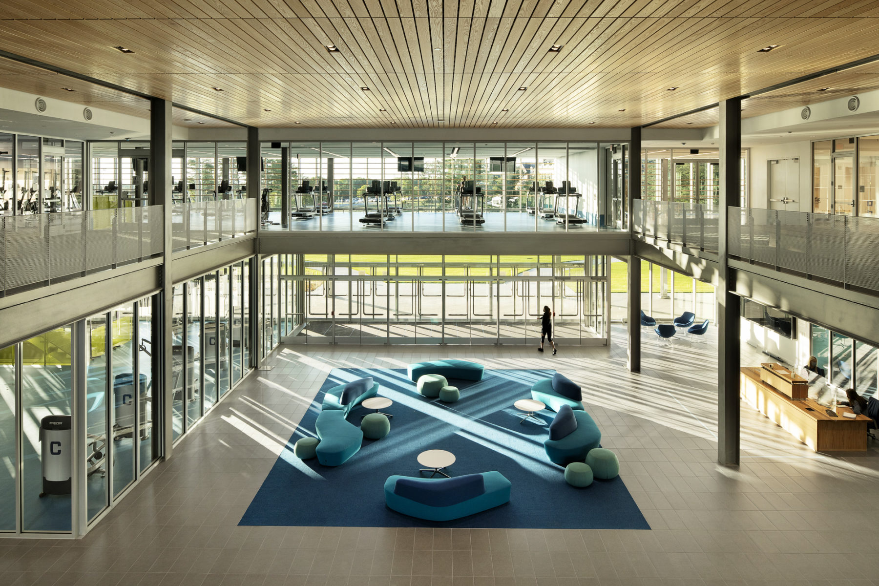 photo of two-story building entry. Light reflects on the ground and a blue carpet and furniture are centered in the space