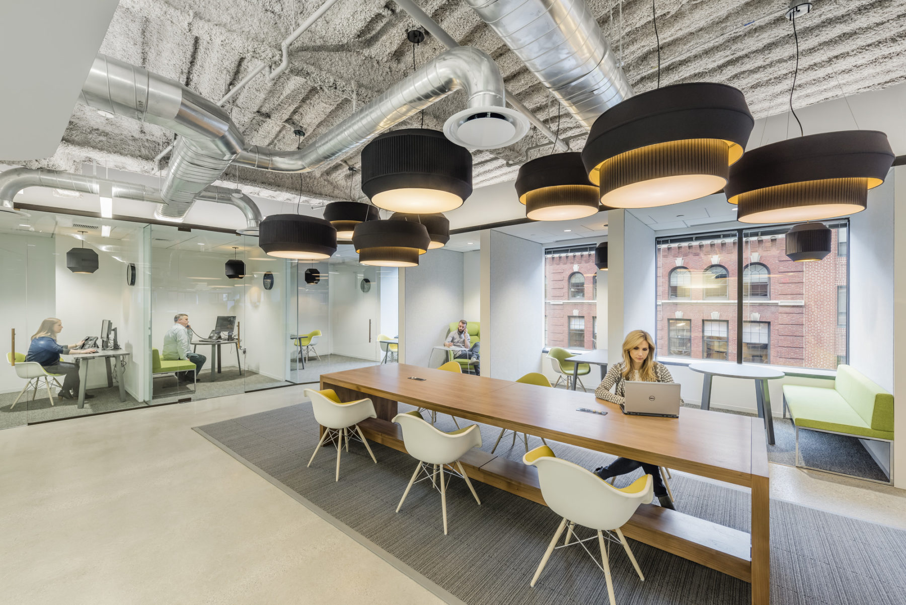 Women sits on long desk working. Four private office spaces towards the back.