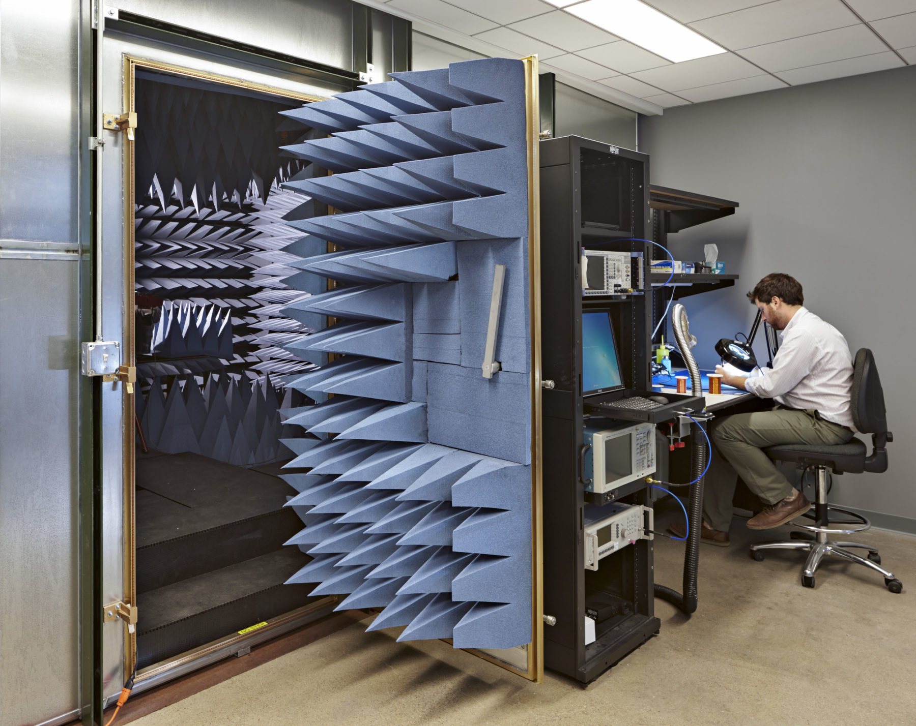 Man working with a microscope/doing research work at his desk and a open vault door on the left.