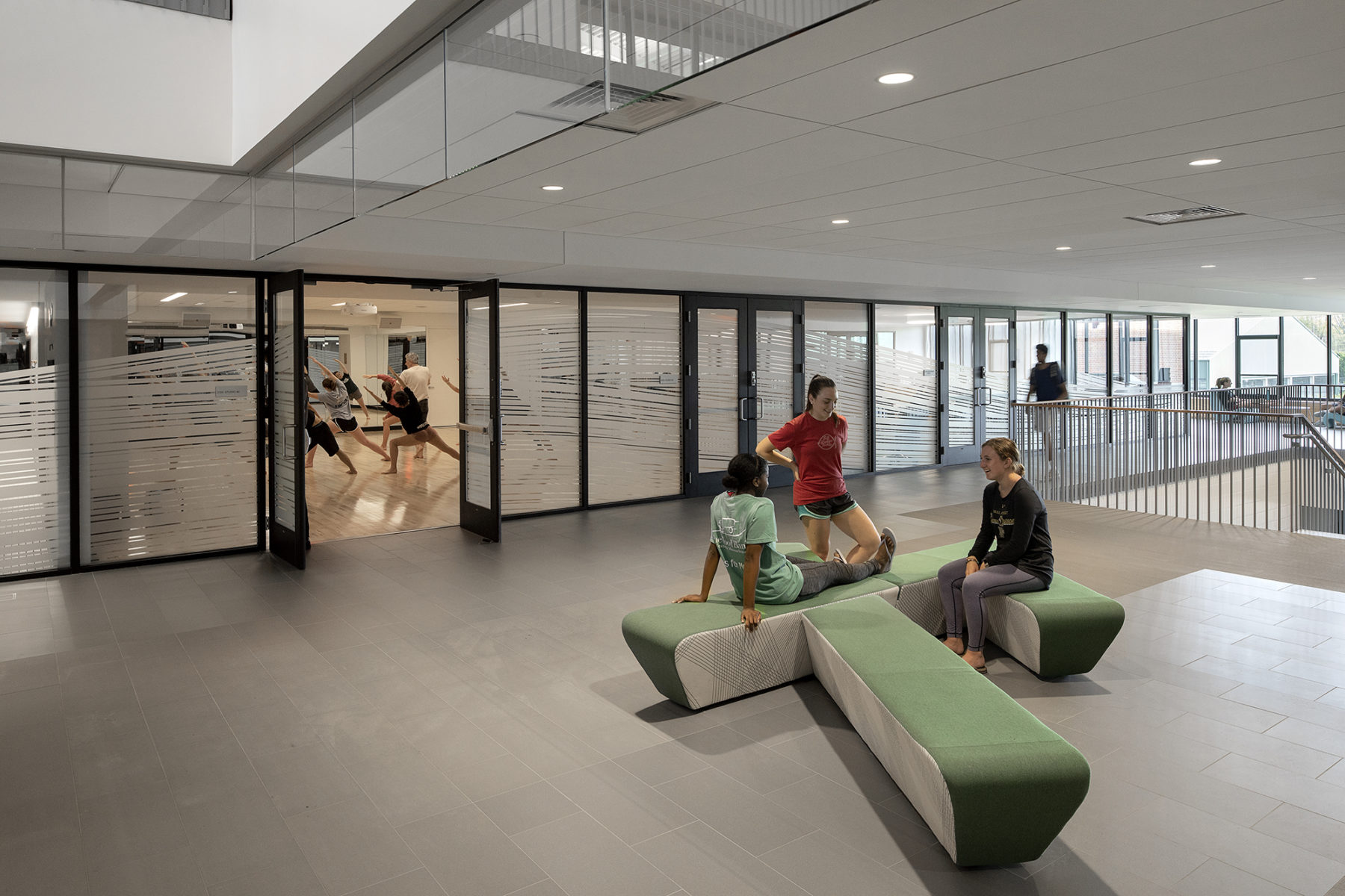 people sitting in lower lobby, yoga class in room beyond