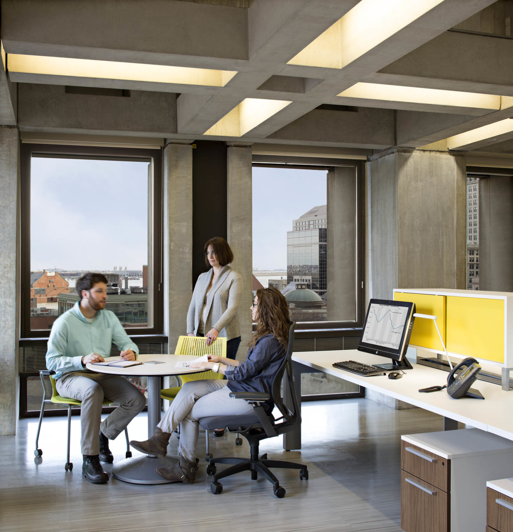 Three people gathered around a table near workstation