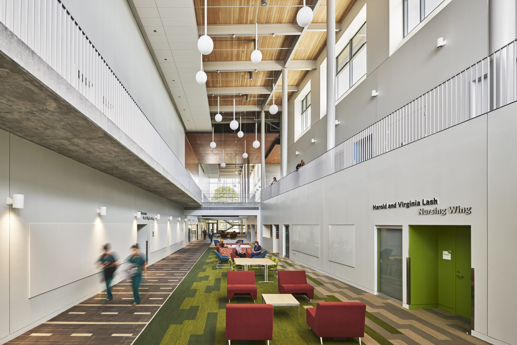 A hallway in the new building that features green carpet and red chairs.