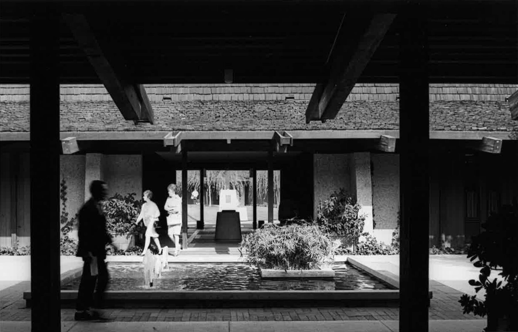 black and white photograph of fountain in courtyard with students walking in foreground and background