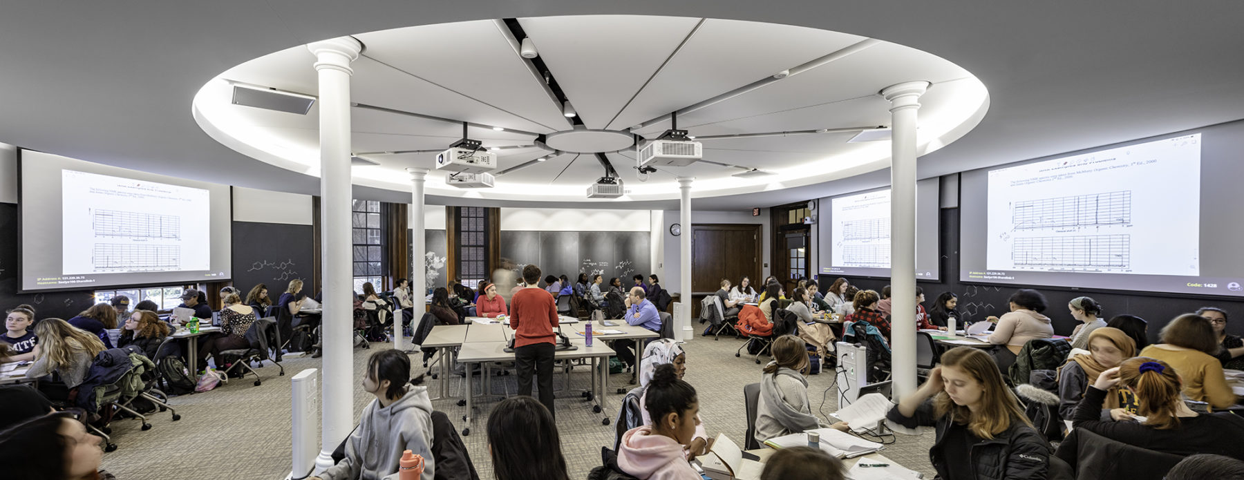 students gathered around circular classroom, chalkboards at perimeter