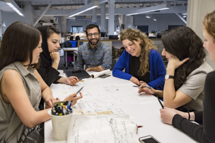 Photo of group gathered around a table discussing the design idea over a drawing