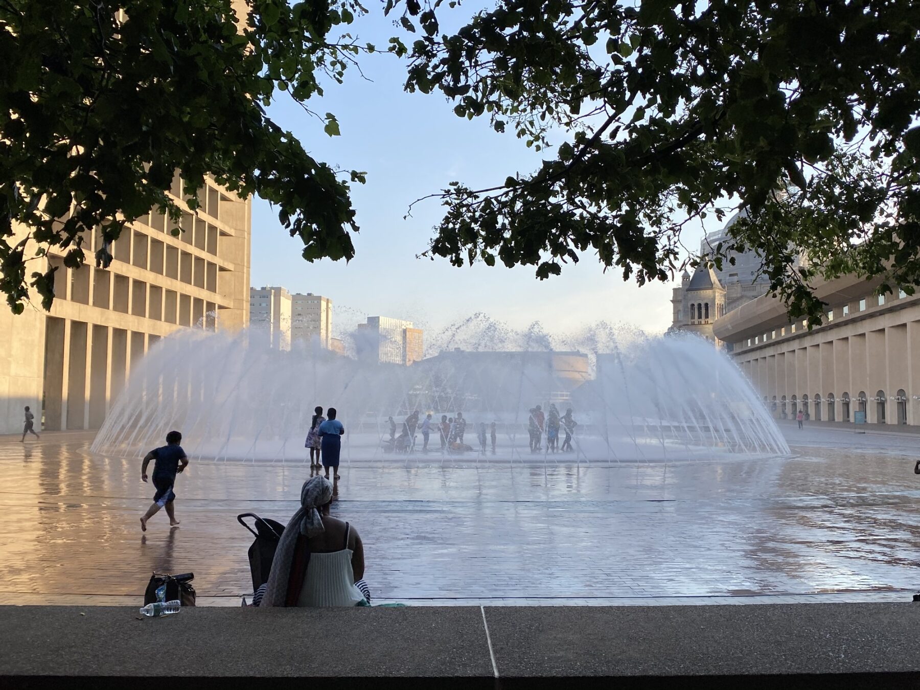 photograph of circular fountain with visitors splashing in the water