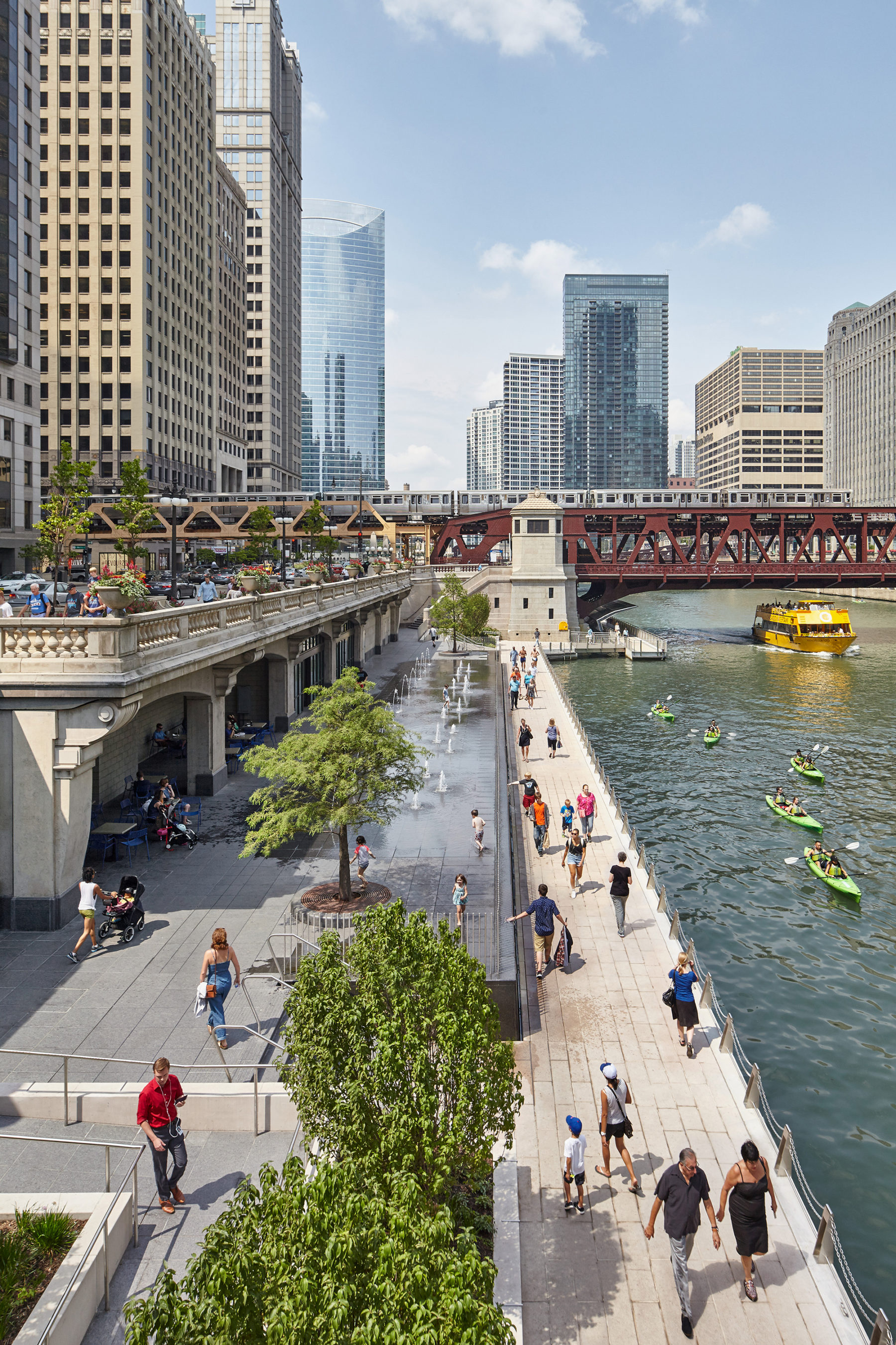 Photograph from the bridge above the Water Plaza looking at people walking along the river