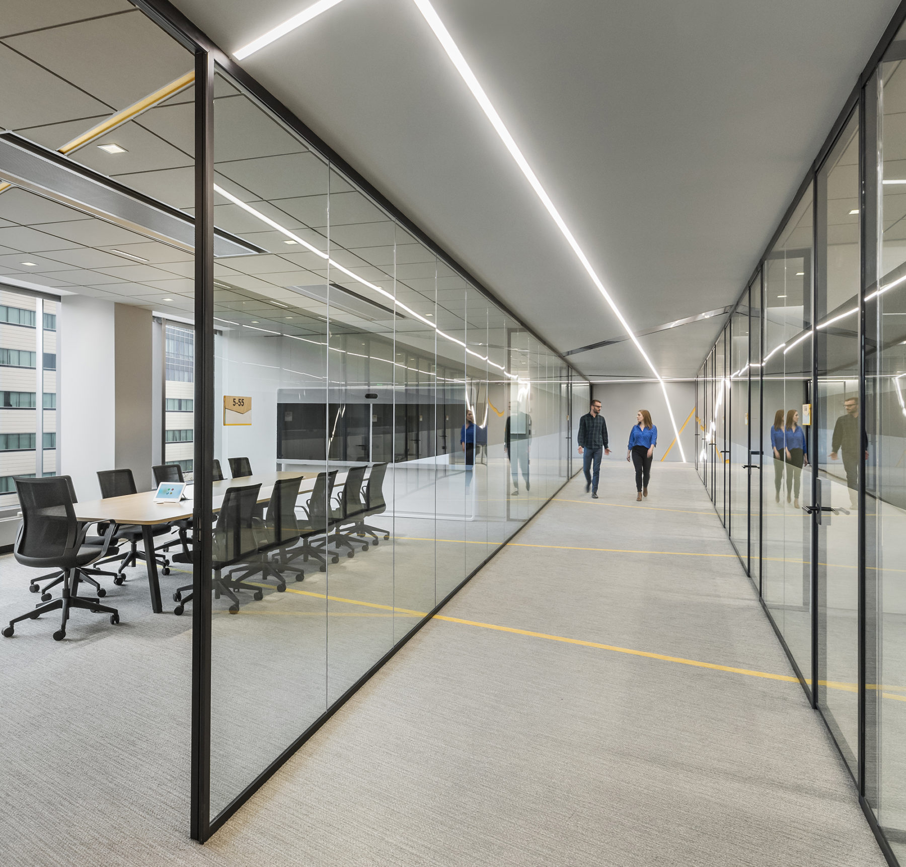 two people walk down a hallway lined with conference rooms