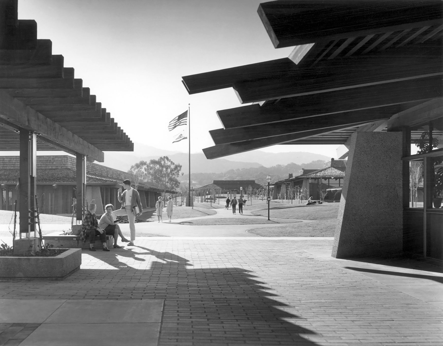 Black and white photo of students sitting in an outdoor courtyard between two buildings
