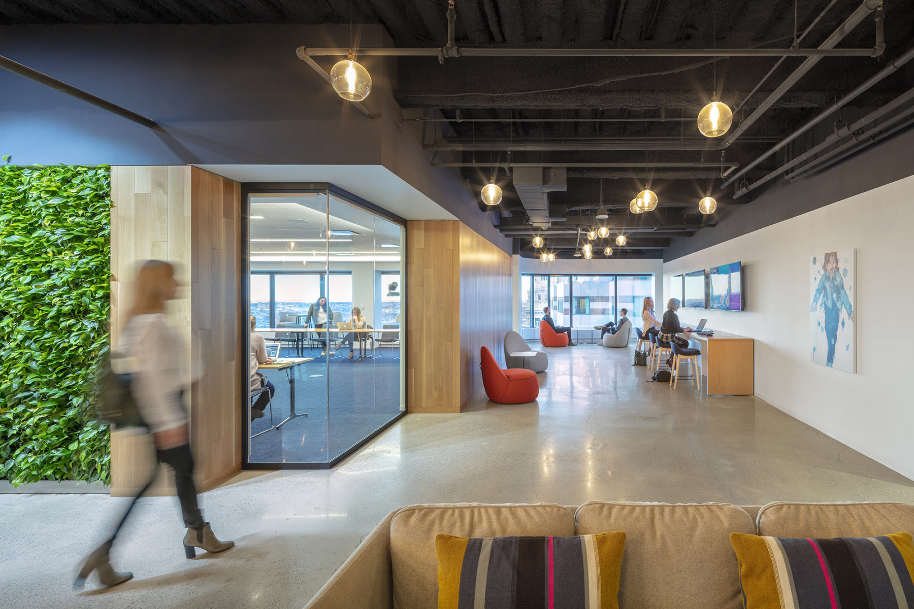 Woman walking in front of conference room, people sitting in the background.