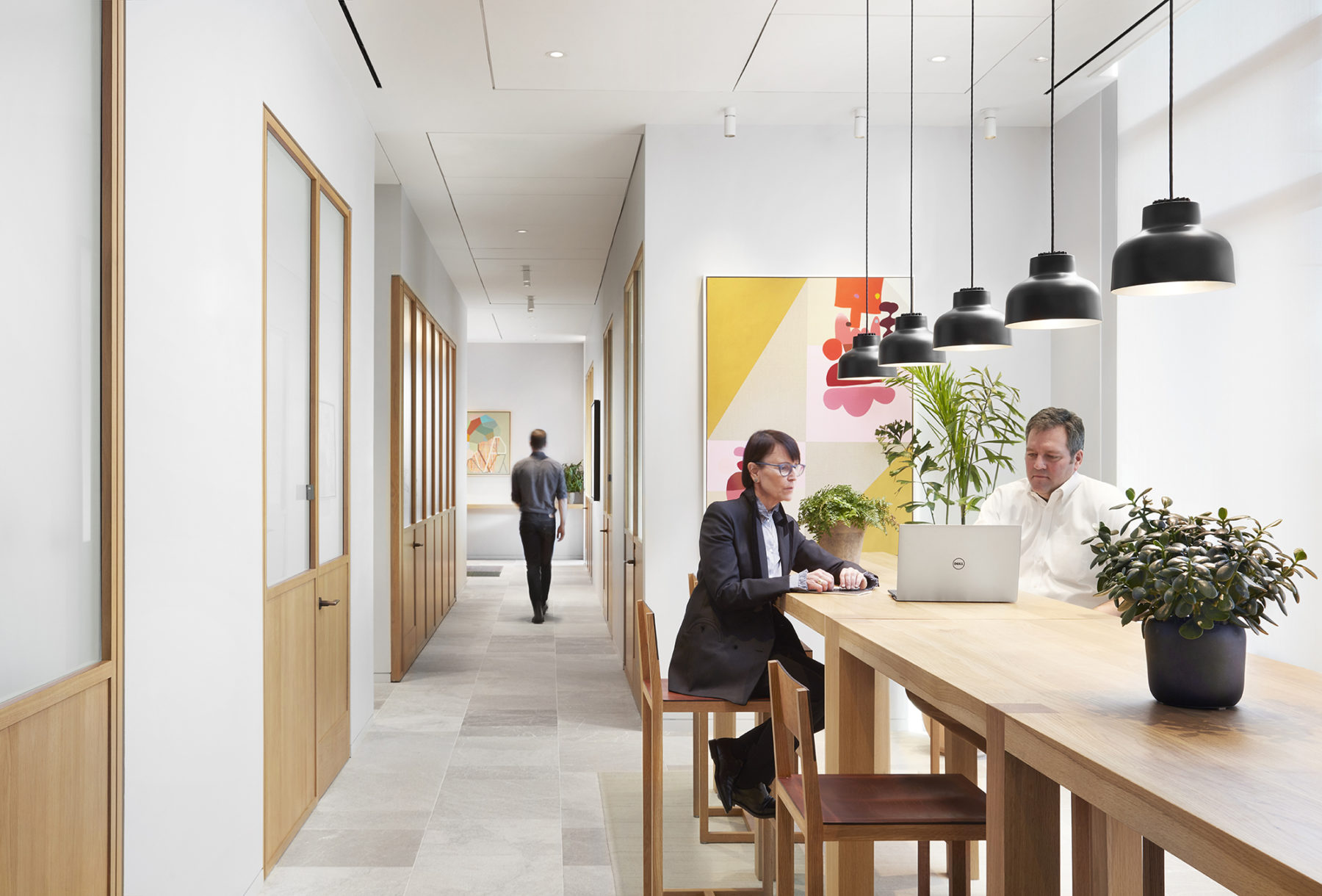 two people working together at table, corridor in background