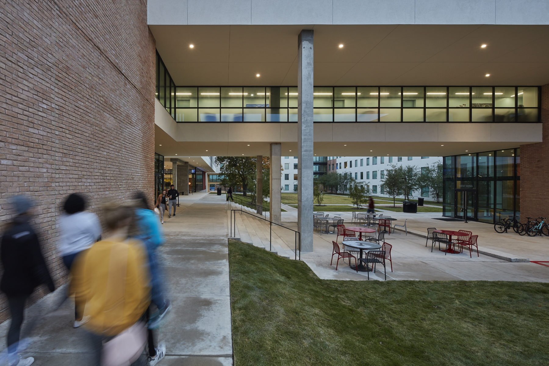 exterior with students walking by, bridge illuminated above