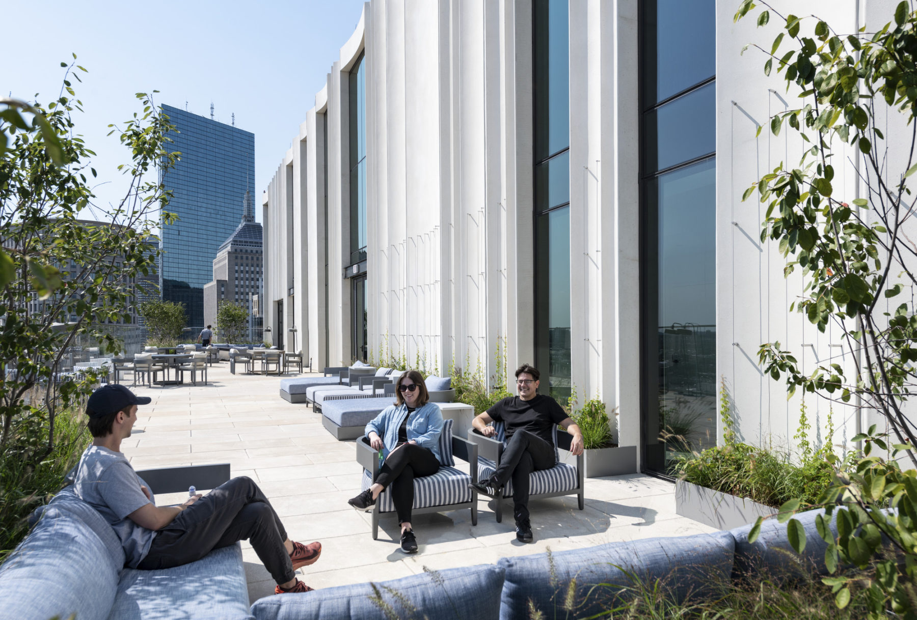 exterior photo of outdoor terrace. three people sit in soft seating in the foreground.