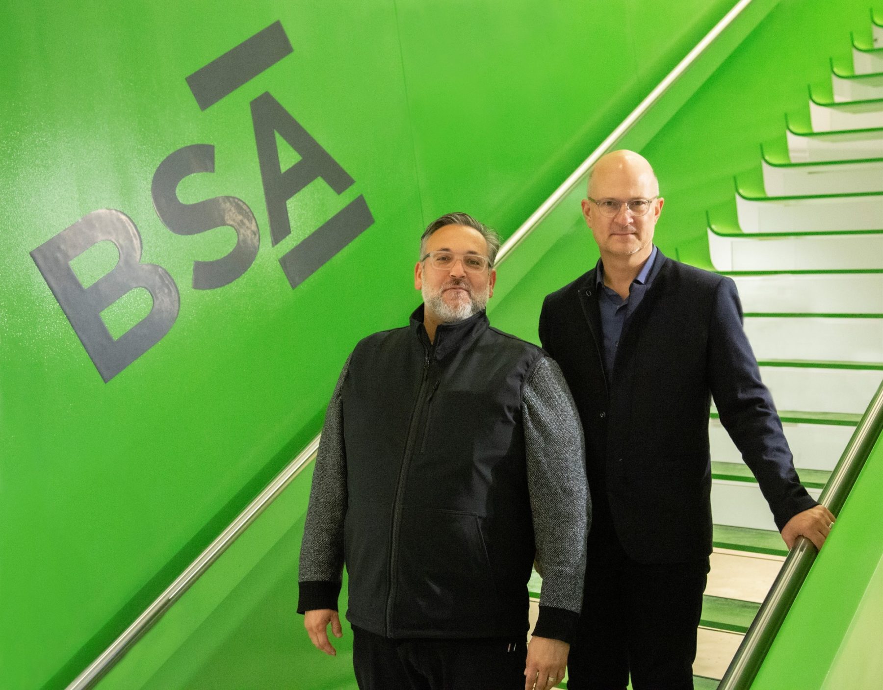 Two people standing on stairs, large BSA logo on wall behind them