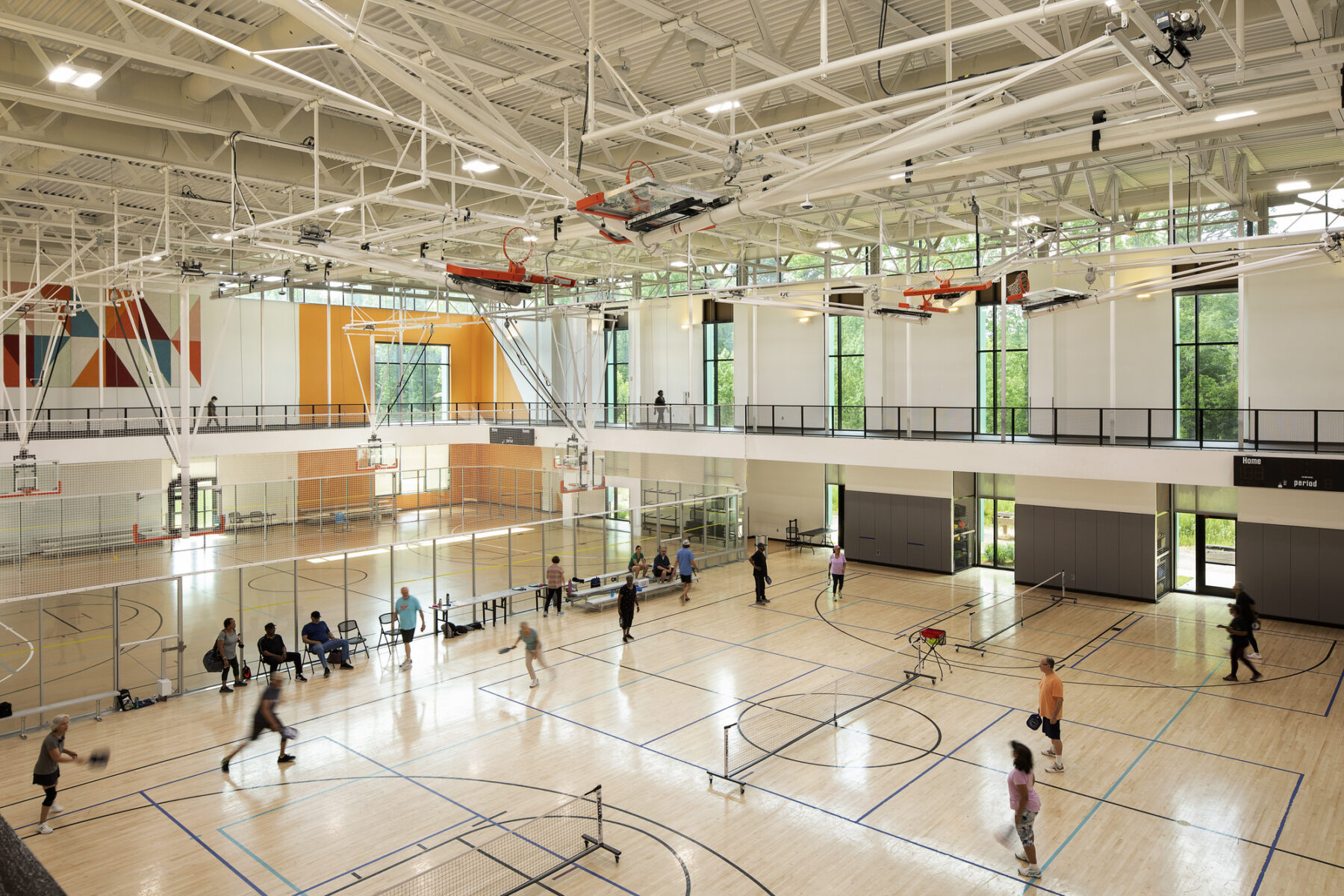 View from up on the indoor track looking down into the open gymnasium courts with natural light in the windows, and boldly colored geometric patterns on the far wall