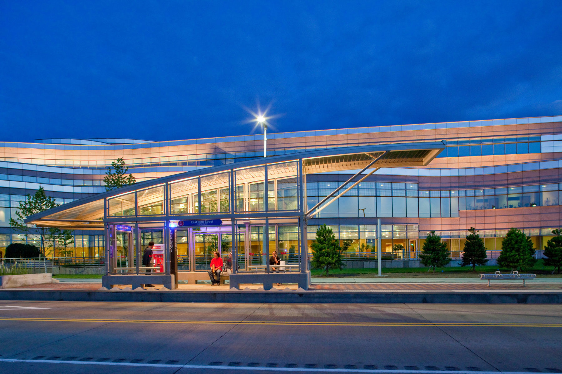 photo of bus stop at night with large building in background