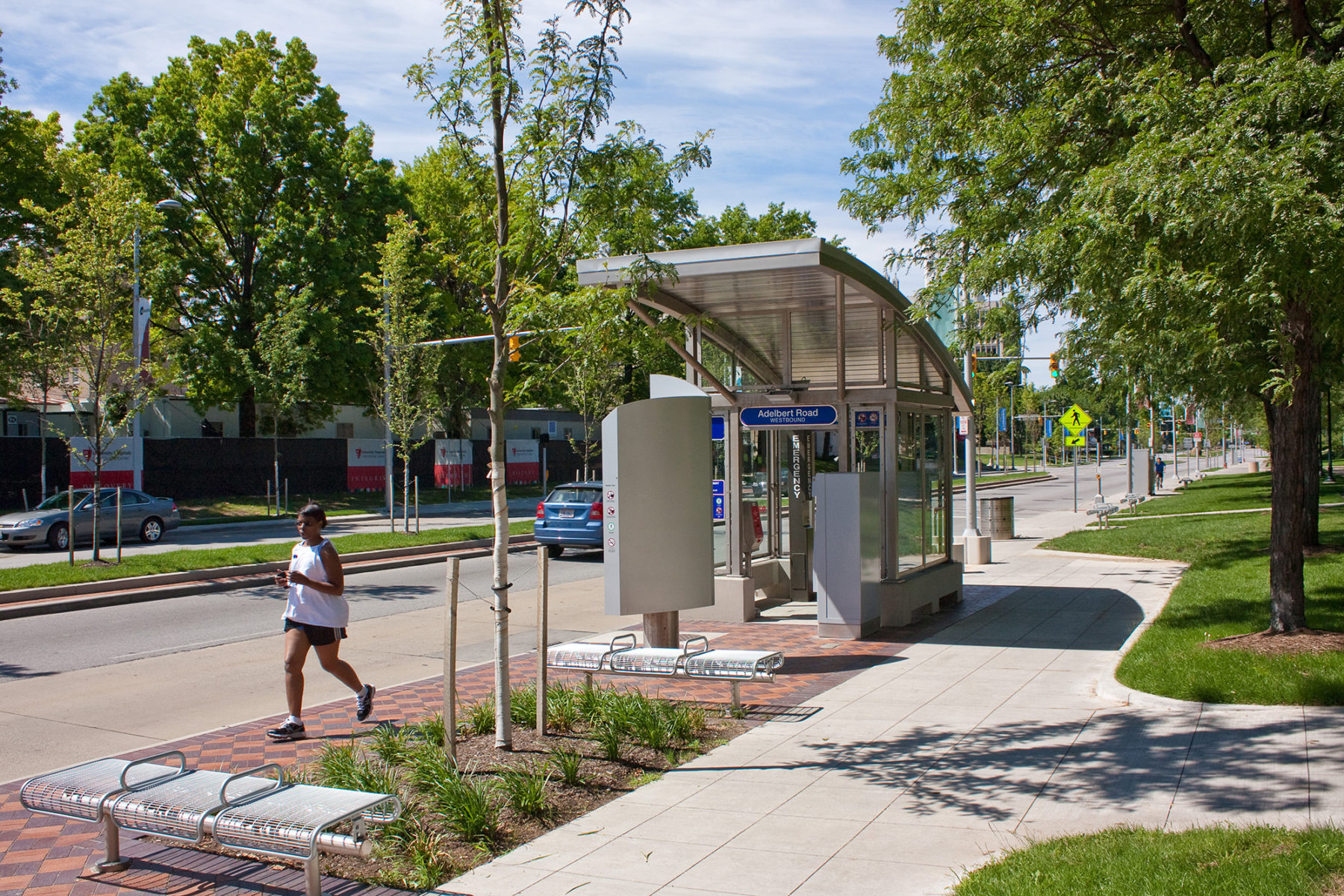 daytime photo of bus stop with runner on sidewalk