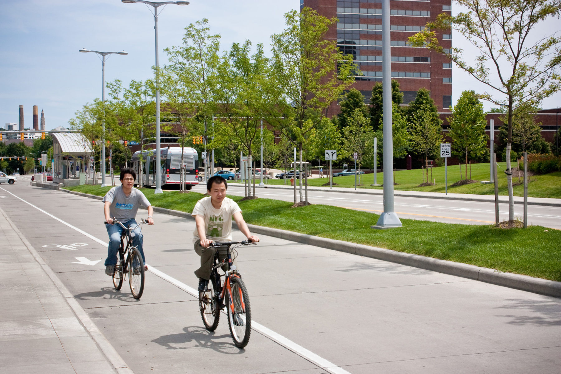 photo of street with grass and trees in median, two bicyclists in bike lane