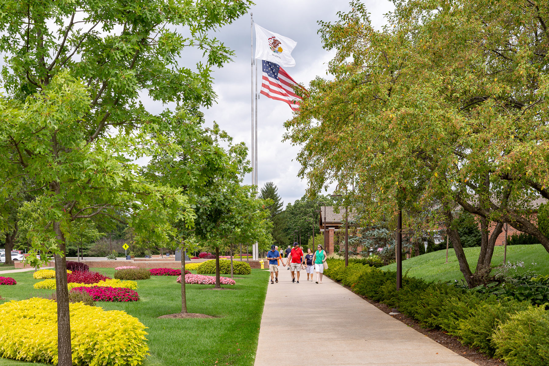 people walk down a paved pathway with an american flag in background