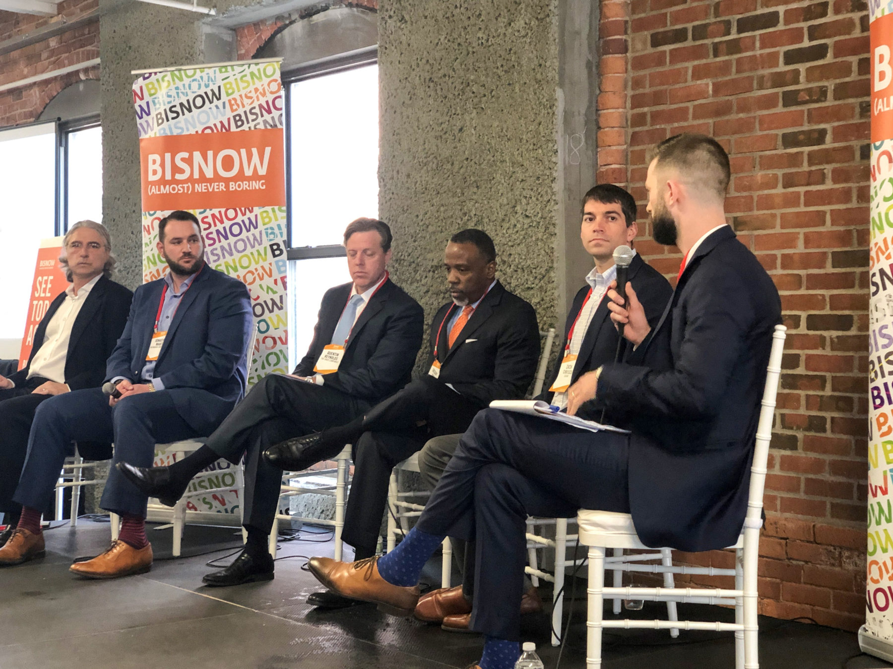 Group of men sitting on a panel. man on far right is speaking