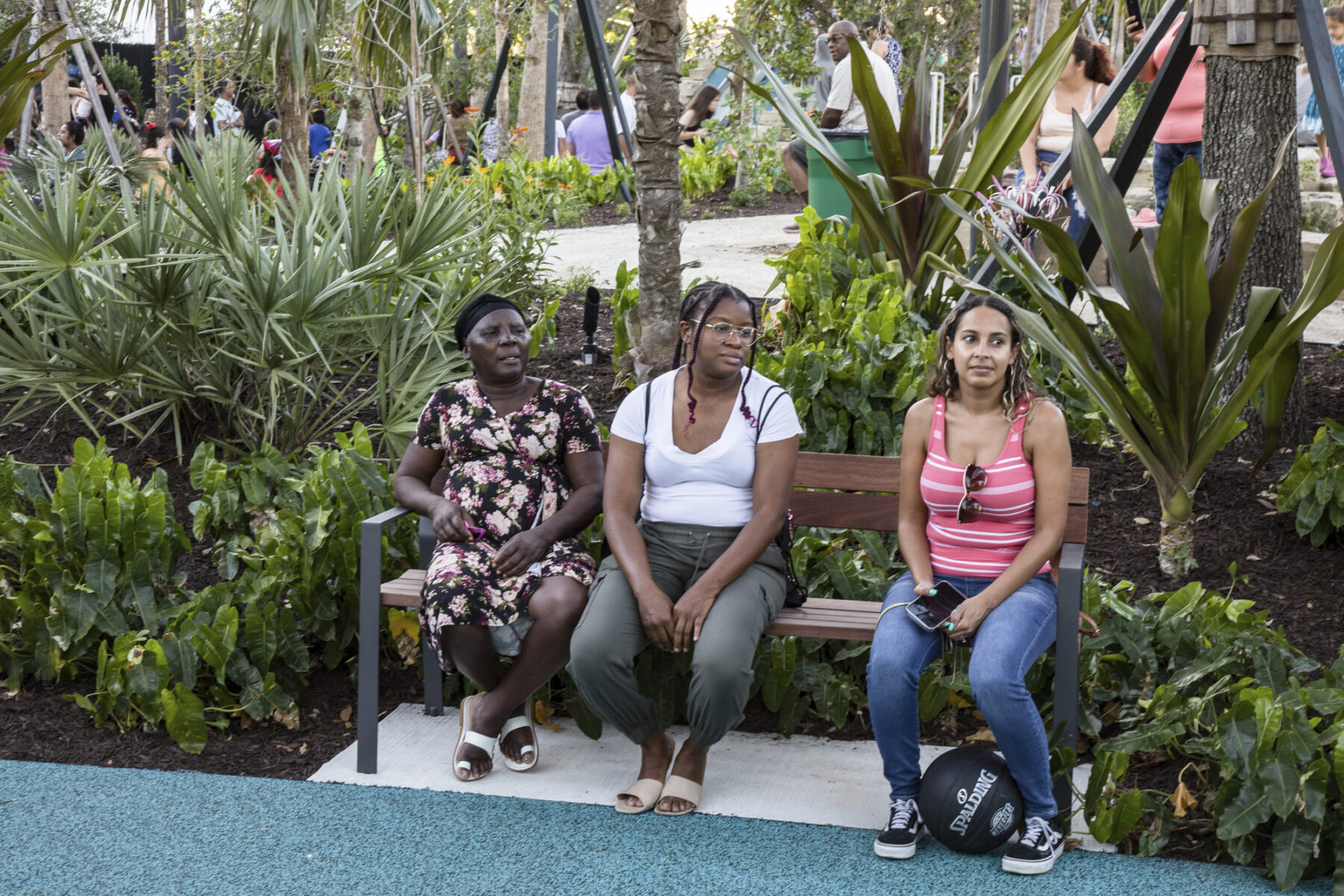 three adults resting in park bench beside native plantings