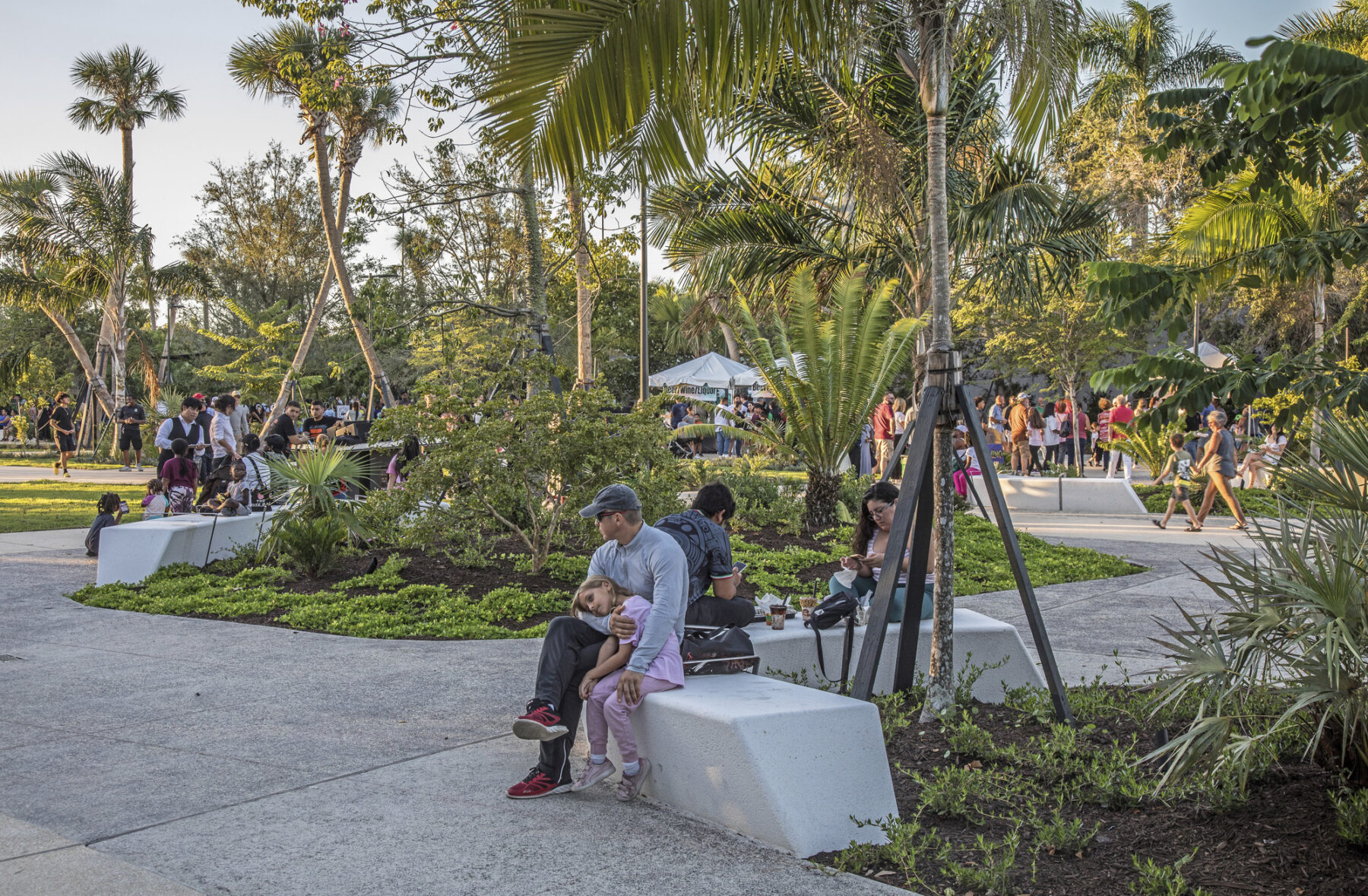 father and child resting on park bench under shaded tree