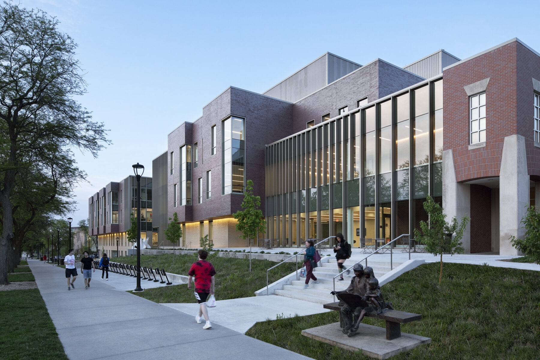 Photo viewing the building exterior at dusk with pedestrians walking along the streetscape and entry plaza