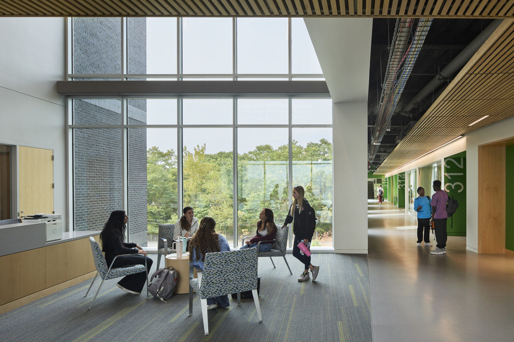 Photo of students gathered at informal seating area with double height windows and view down the corridor with natural light flooding in
