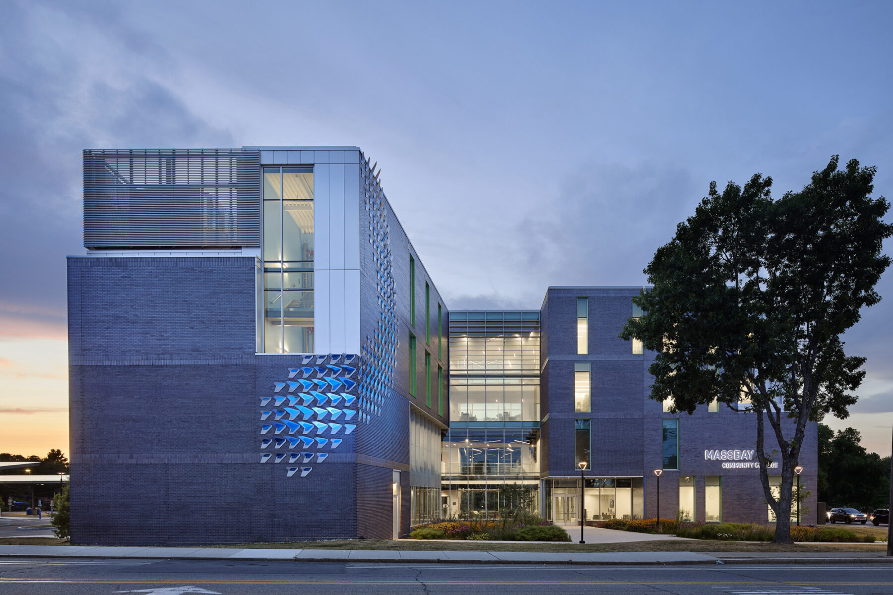 Exterior elevational view at dusk from the road facing the building entrance with illuminated sculpture on the corner facade