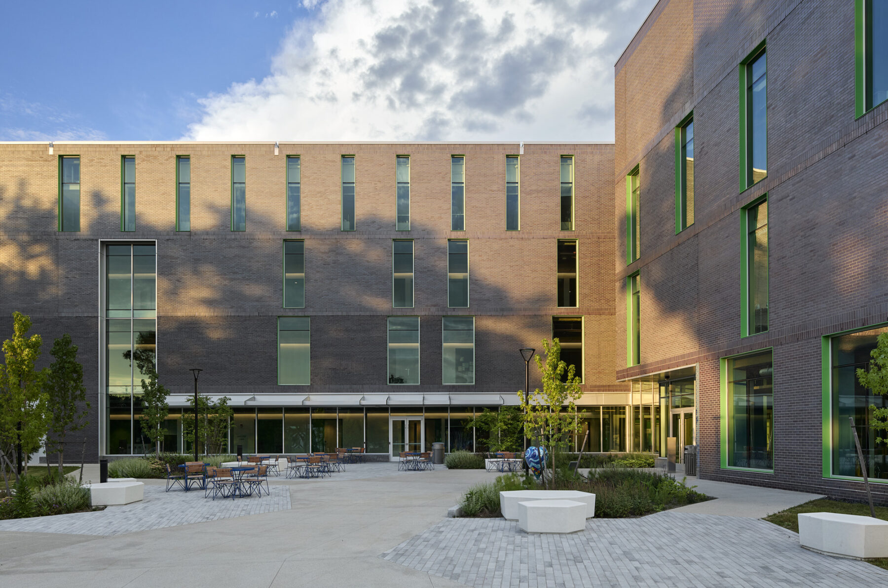Exterior elevational view of the building and terrace with tables and lush plantings