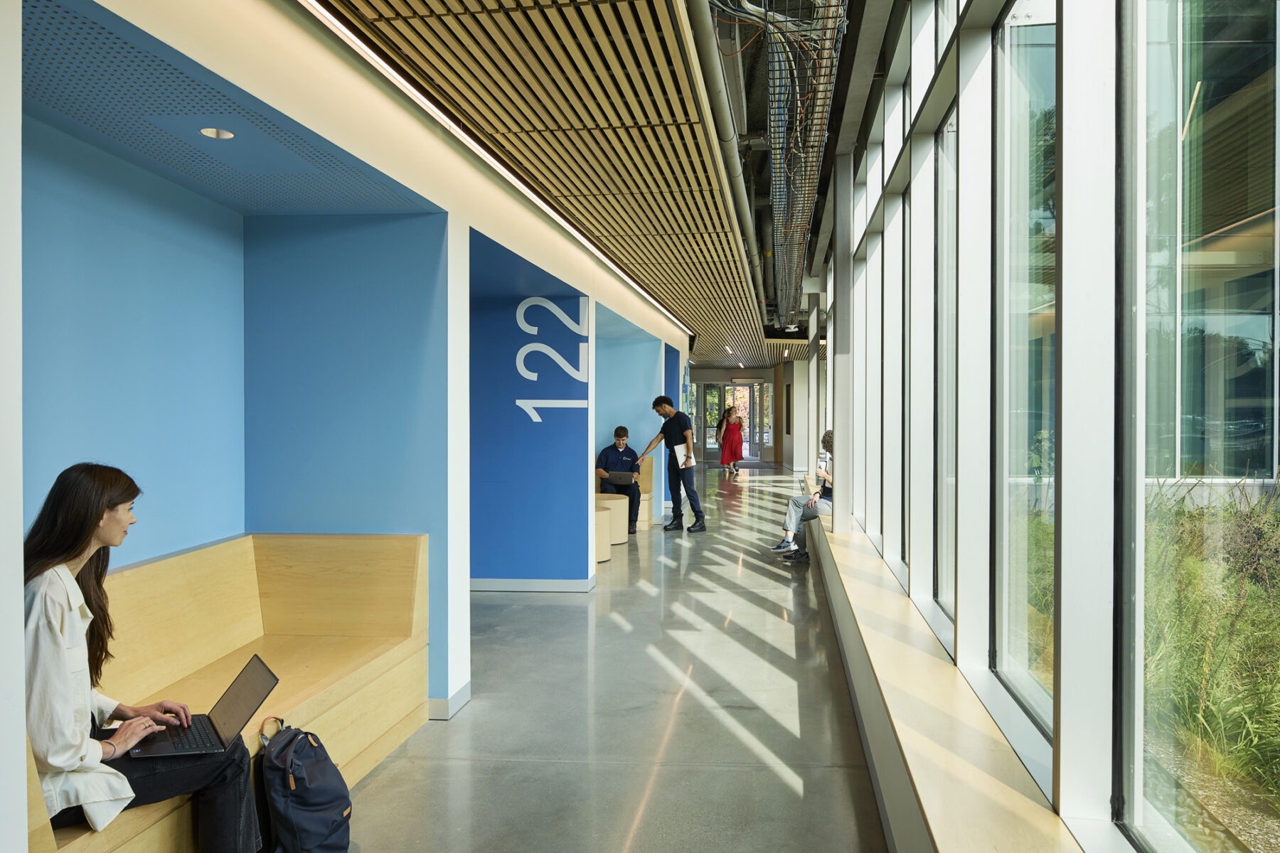 View looking down ground floor corridor with benches situated in nooks along the hallways and floor to ceiling windows on the opposite wall allowing daylight to stream in