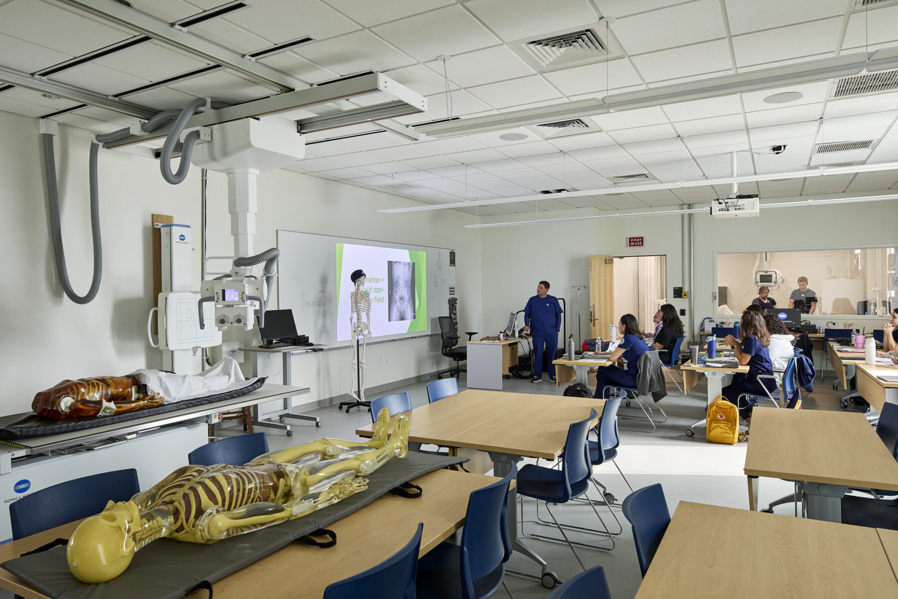 Radiology classroom with large x-ray machine, skeletons, and students at desks during a lecture presentation