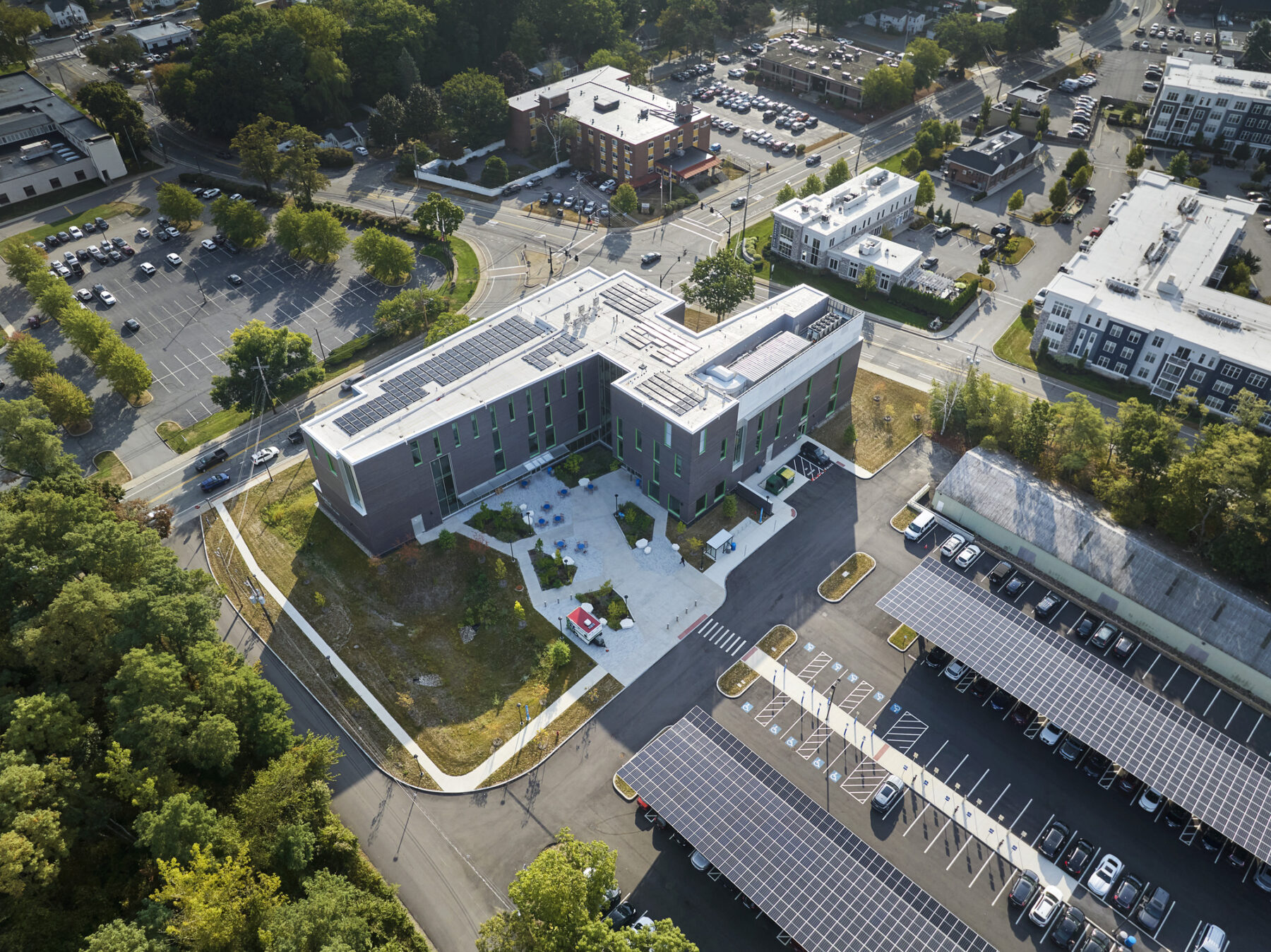 Aerial view of building with solar panels on roof and above parking lot