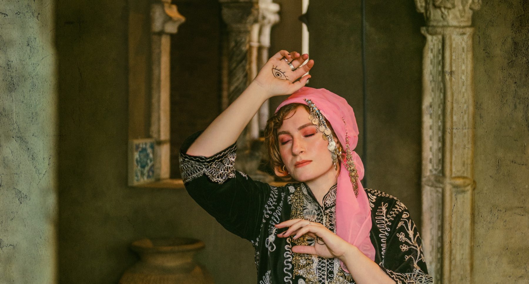 Photo of the artist, Feda Eid, with her hand raised above her head and her eyes closed, in the Isabella Stuart Gardner Museum